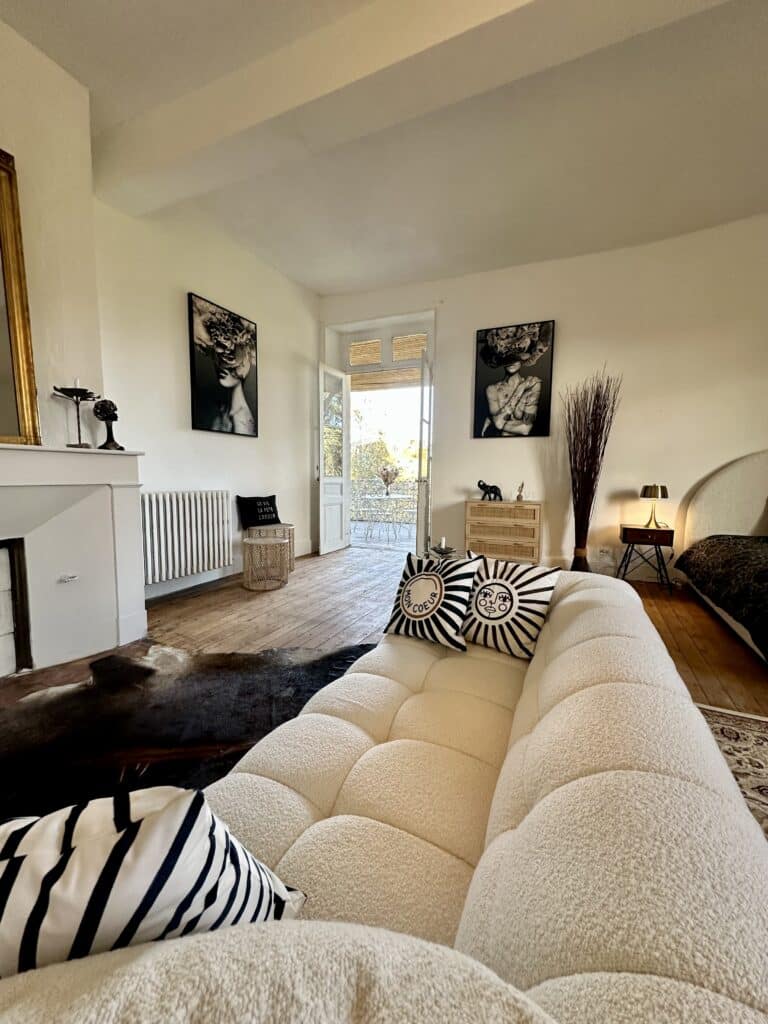 Canapé Bouclé Crème : Décoration Salon Chic et Bohème Canapé bouclé crème dans un salon bohème chic. Coussins graphiques "MON COEUR" et art floral noir/blanc. Pièce lumineuse avec portes-fenêtres.