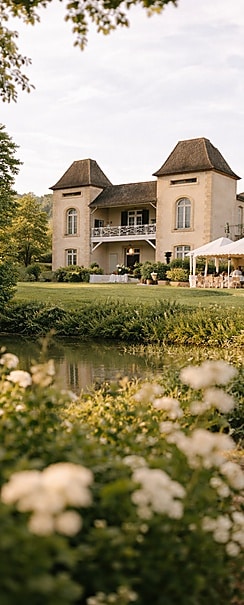 Château de charme pour une réception de mariage élégante. Romantique château à tourelles en pierre claire. Réception élégante dans le jardin près de l'étang. Belles fleurs blanches au premier plan.