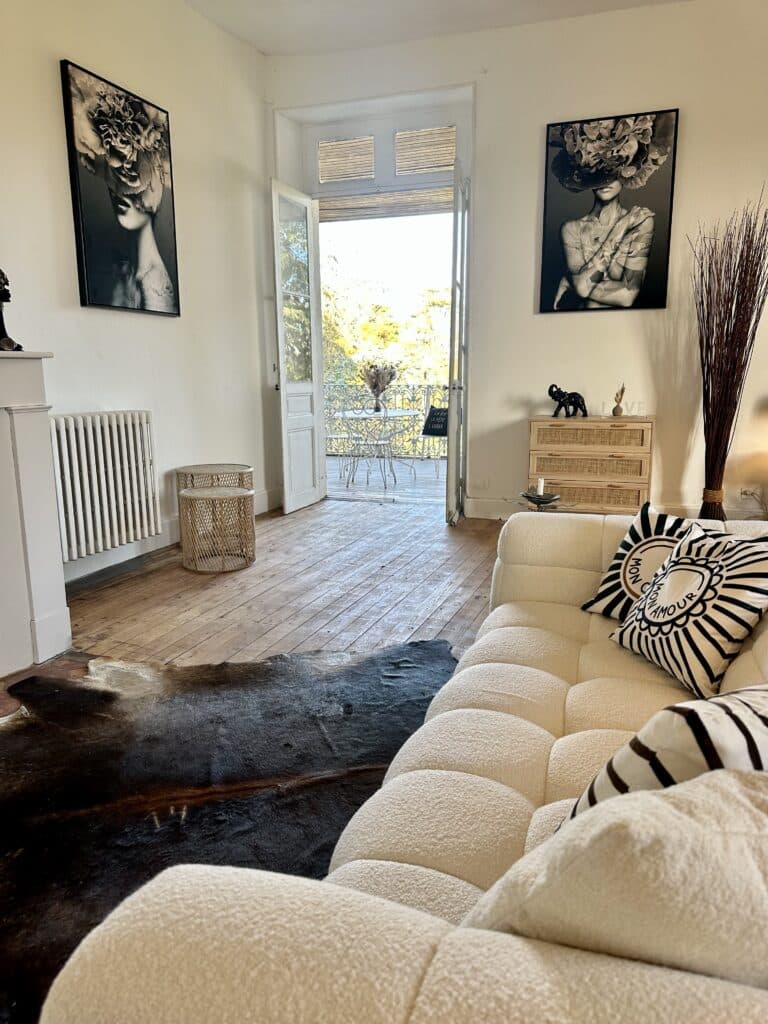 Canapé bouclé blanc et décor bohème avec vue balcon Salon bohème chic: canapé bouclé blanc, tapis en peau de vache sur plancher bois. Portes ouvertes sur balcon. Art N&B et coussins "MON AMOUR".