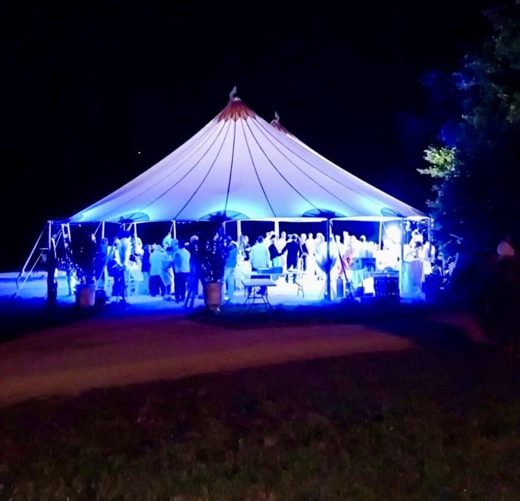 Chapiteau de réception illuminé pour soirée festive Chapiteau blanc illuminé de bleu lors d'une fête nocturne avec invités en extérieur.